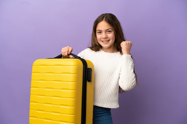Petite fille caucasienne isolée sur fond violet en vacances avec valise de voyage
