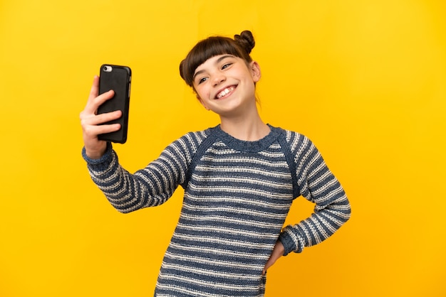 Petite fille caucasienne isolée sur jaune faisant un selfie