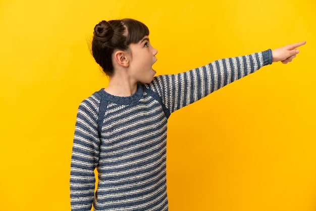 Petite fille caucasienne isolée sur jaune pointant vers l'extérieur