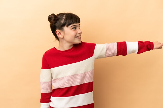 Petite fille caucasienne isolée sur un mur beige donnant un geste de pouce en l'air