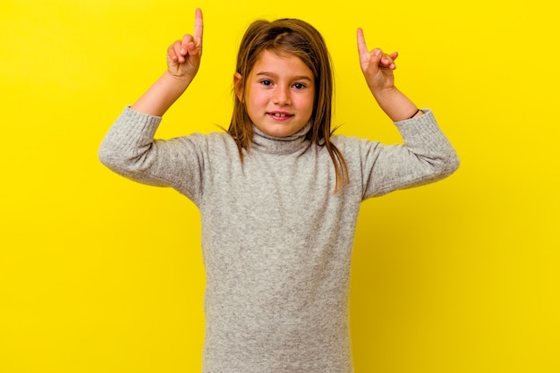 Petite fille caucasienne isolée sur un mur jaune indique avec les deux doigts avant montrant un espace vide.