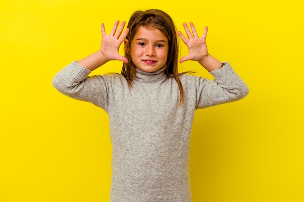 Petite fille caucasienne isolée sur un mur jaune montrant le numéro dix avec les mains.