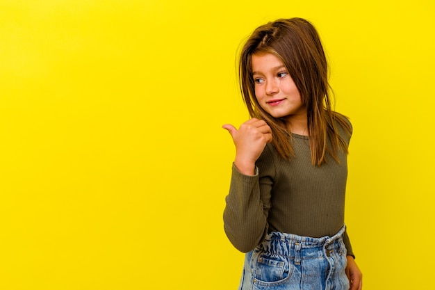 Petite fille caucasienne isolée sur des points de fond jaune avec le pouce loin, riant et insouciant.