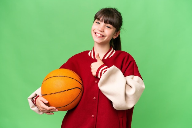 Petite fille caucasienne jouant au basket-ball sur fond isolé donnant un geste du pouce levé
