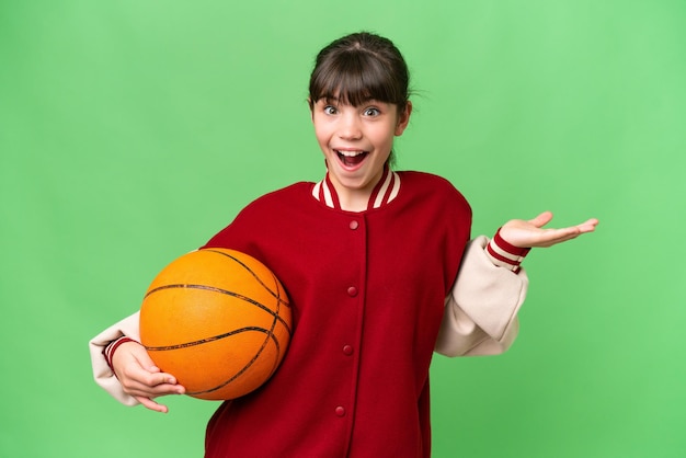 Petite fille caucasienne jouant au basket-ball sur fond isolé avec une expression faciale choquée