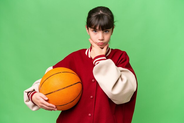 Petite fille caucasienne jouant au basket-ball sur fond isolé pensant