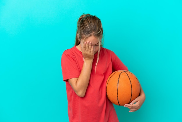 Petite fille caucasienne jouant au basket-ball isolée sur fond bleu avec une expression fatiguée et malade