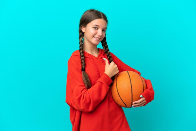 Petite fille caucasienne jouant au basket isolée sur fond bleu fière et satisfaite