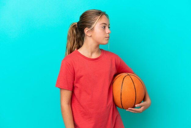 Petite fille caucasienne jouant au basket isolée sur fond bleu regardant sur le côté