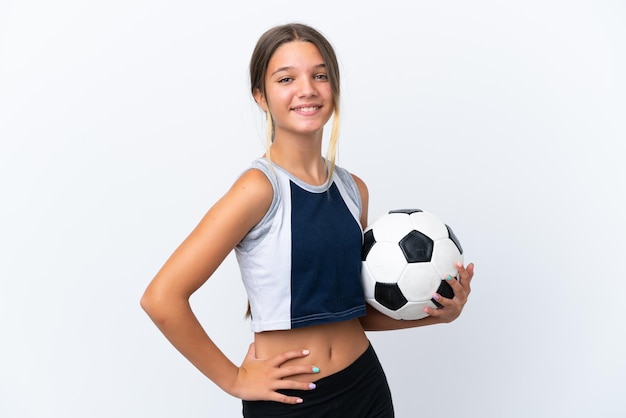 Petite fille caucasienne jouant au football isolé sur fond blanc posant avec les bras à la hanche et souriant