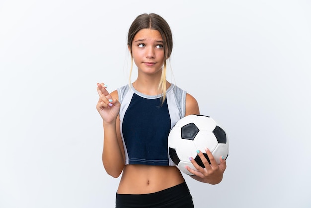 Petite fille caucasienne jouant au football isolée sur fond blanc avec les doigts croisés et souhaitant le meilleur