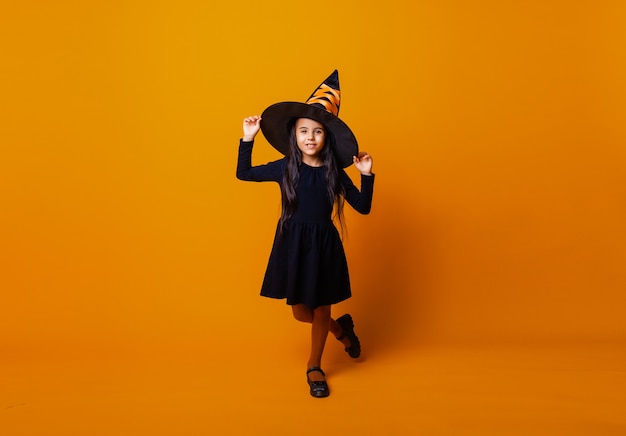 Petite fille caucasienne joyeuse en costume de sorcière Halloween isolée sur fond jaune.