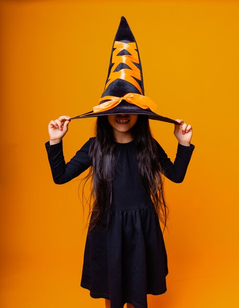 Photo petite fille caucasienne joyeuse en costume de sorcière halloween isolée sur fond jaune.