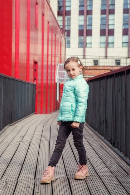 Petite fille caucasienne mignonne posant sur un pont en bois entre les bâtiments colorés modernes regardant la caméra