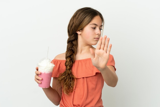 Petite fille caucasienne avec milk-shake aux fraises isolé sur fond blanc faisant un geste d'arrêt et déçu