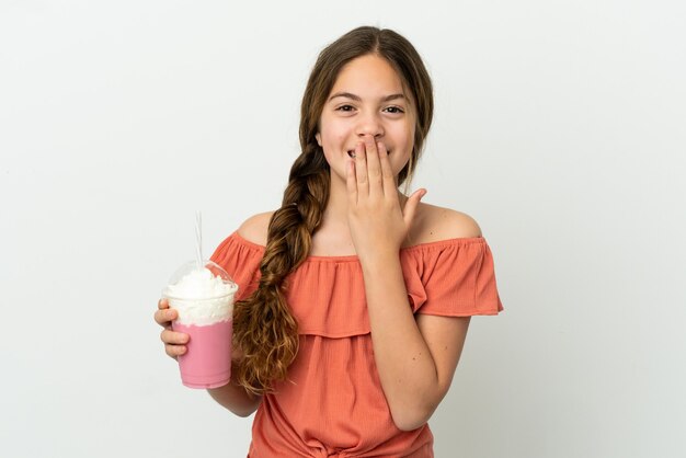 Petite fille caucasienne avec milk-shake aux fraises isolé sur fond blanc heureux et souriant couvrant la bouche avec la main