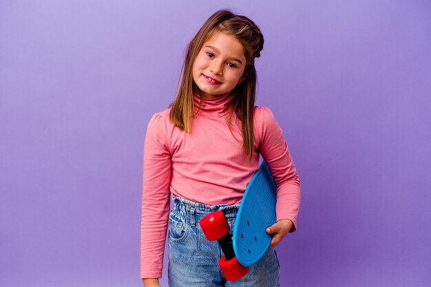 Petite fille caucasienne patineuse isolée sur mur bleu heureux, souriant et joyeux.