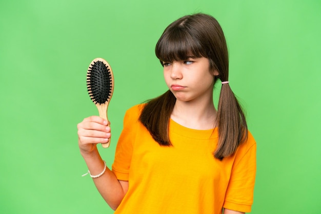 Petite fille caucasienne avec un peigne à cheveux sur fond isolé avec une expression triste