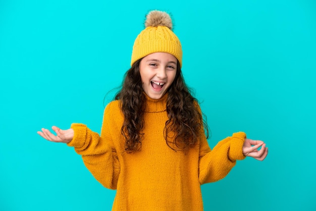 Petite fille caucasienne portant un chapeau d'hiver isolé sur fond bleu avec une expression faciale choquée