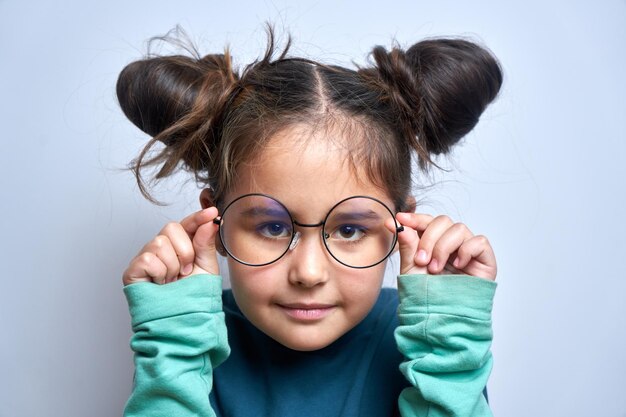 Petite fille caucasienne portant des lunettes louchant tout en regardant la caméra isolée sur fond blanc Concept de problèmes de vision