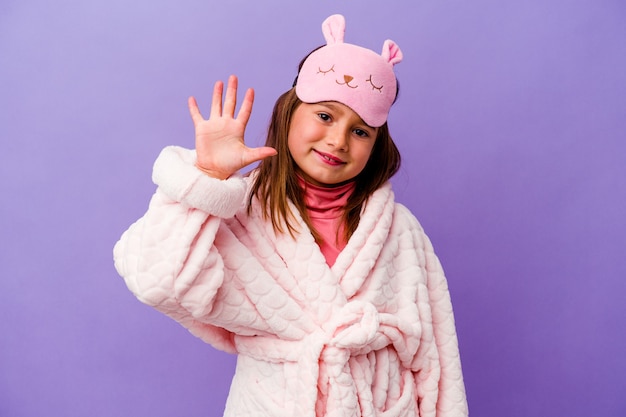 Petite fille caucasienne portant un pyjama isolé sur un mur violet souriant joyeux montrant le numéro cinq avec les doigts.