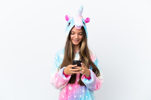 Petite fille caucasienne portant un pyjama licorne isolé sur fond blanc en envoyant un message avec le mobile