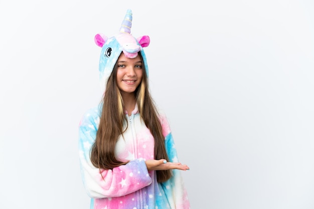 Petite fille caucasienne portant un pyjama licorne isolé sur fond blanc présentant une idée tout en regardant en souriant vers