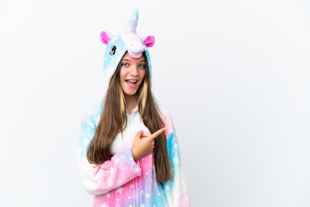 Petite fille caucasienne portant un pyjama de licorne isolé sur fond blanc surpris et pointant le côté