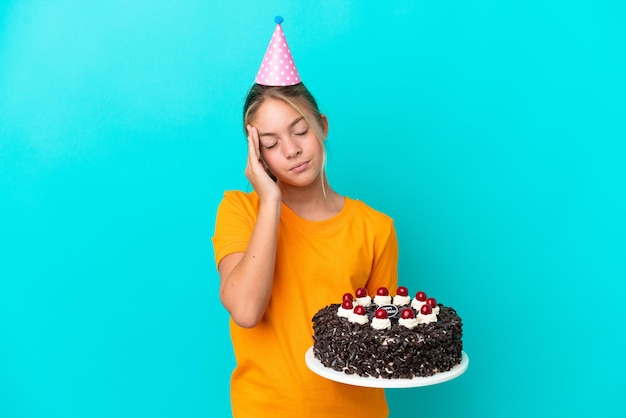 Petite fille caucasienne tenant un gâteau d'anniversaire isolé sur fond bleu avec des maux de tête