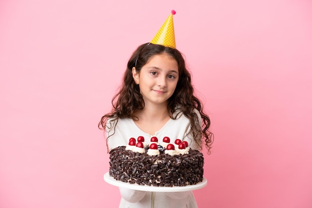 Petite fille caucasienne tenant un gâteau d'anniversaire isolé sur fond rose