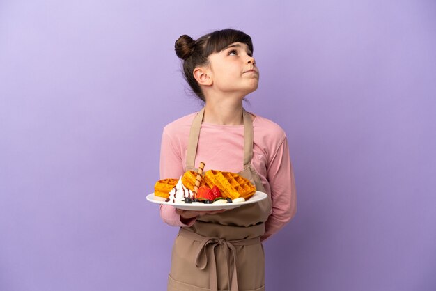 Petite fille caucasienne tenant des gaufres isolées sur violet et levant