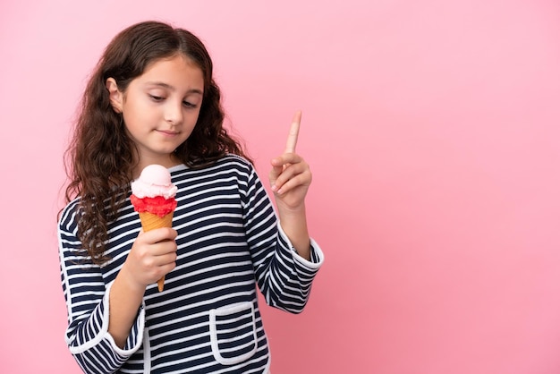 Petite fille caucasienne tenant une glace isolée sur fond rose dans l'intention de réaliser la solution tout en levant un doigt