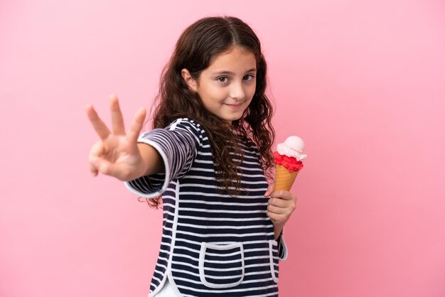 Petite fille caucasienne tenant une glace isolée sur fond rose heureuse et comptant trois avec les doigts