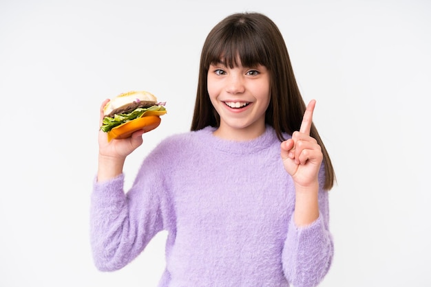 Petite fille caucasienne tenant un hamburger sur fond isolé pointant vers le haut une excellente idée