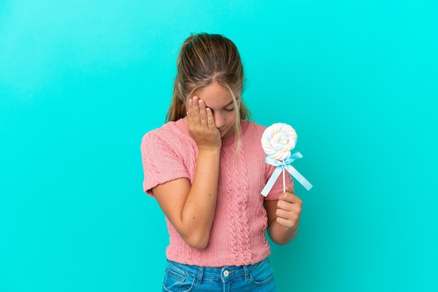 Petite fille caucasienne tenant une sucette isolée sur fond bleu avec une expression fatiguée et malade