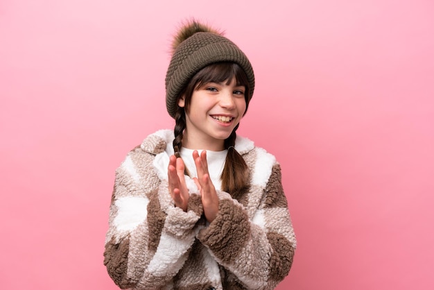 Petite fille caucasienne avec veste d'hiver isolée sur fond rose applaudissant après présentation lors d'une conférence