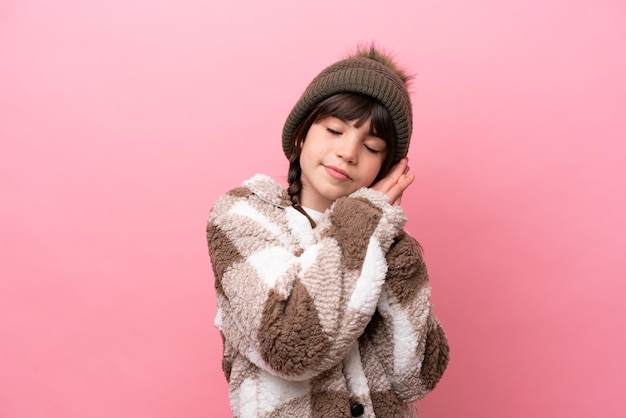 Petite fille caucasienne avec veste d'hiver isolée sur fond rose faisant un geste de sommeil dans une expression dorable