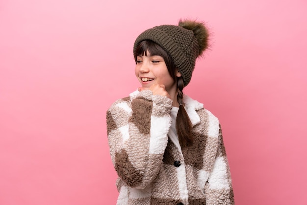 Petite fille caucasienne avec veste d'hiver isolée sur fond rose regardant sur le côté