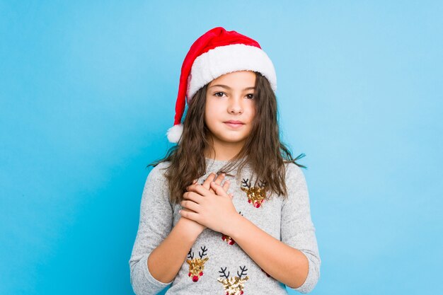 Petite fille célébrant le jour de Noël a une expression amicale, appuyant paume contre la poitrine. Concept de l'amour