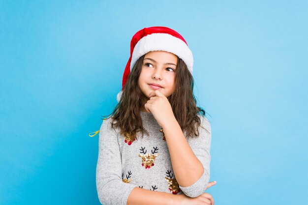 Petite fille célébrant le jour de Noël regardant de côté avec une expression douteuse et sceptique.