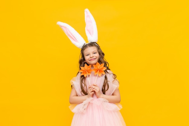 Une petite fille célèbre Pâques Un enfant souriant heureux tient des fleurs d'origami Un charmant adolescent avec des oreilles de lapin sur un fond isolé jaune