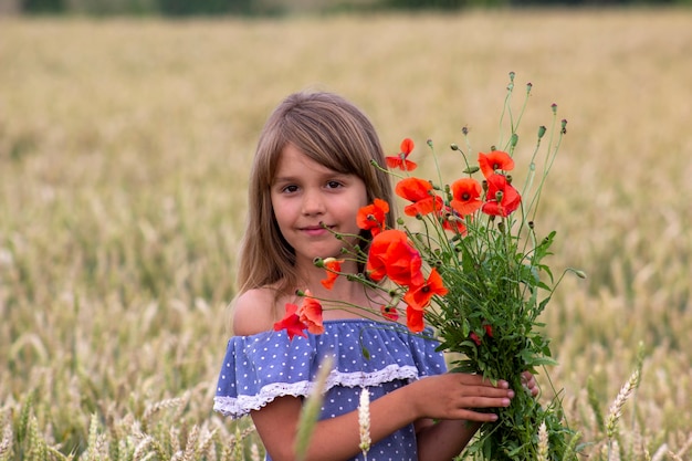 Petite fille sur un champ de blé avec des coquelicots rouges.