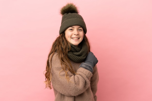 Petite fille avec chapeau d'hiver isolé sur fond rose célébrant une victoire