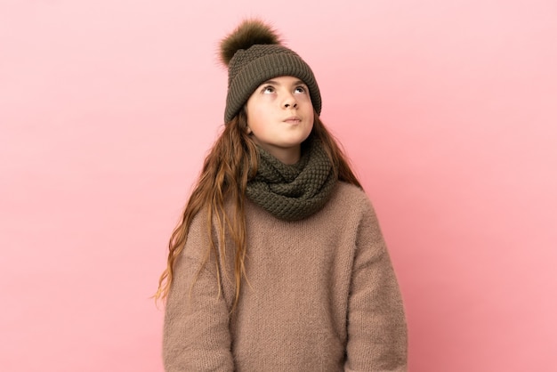 Petite fille avec chapeau d'hiver isolé sur fond rose et levant