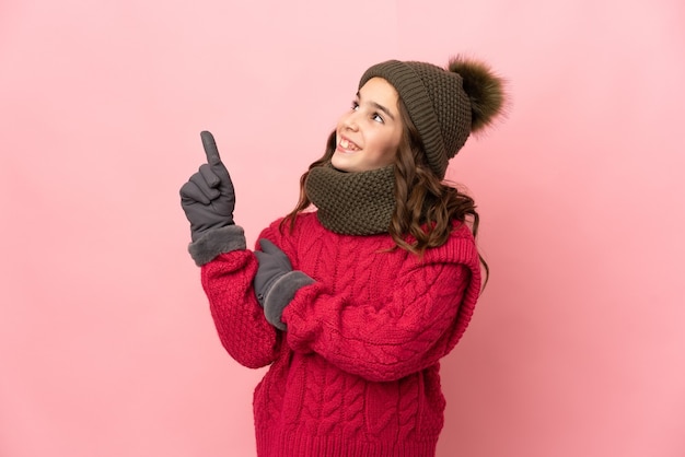 Petite fille avec chapeau d'hiver isolé sur fond rose pointant vers le haut une excellente idée