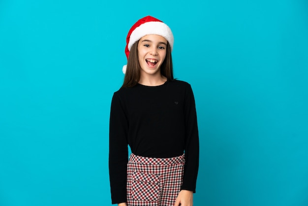 Petite fille avec un chapeau de Noël isolé sur fond bleu avec une expression faciale surprise