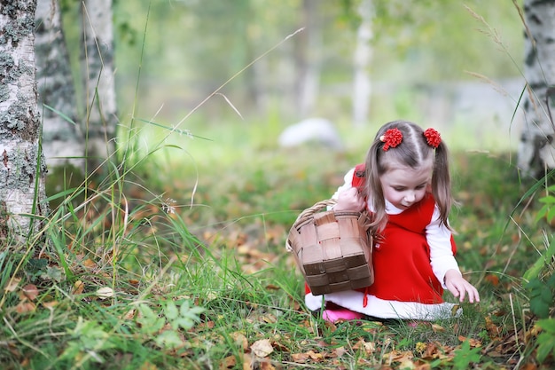 Une petite fille avec un chapeau rouge et des robes marche dans le parc. Cosplay pour le héros de conte de fées "Le petit chaperon rouge"