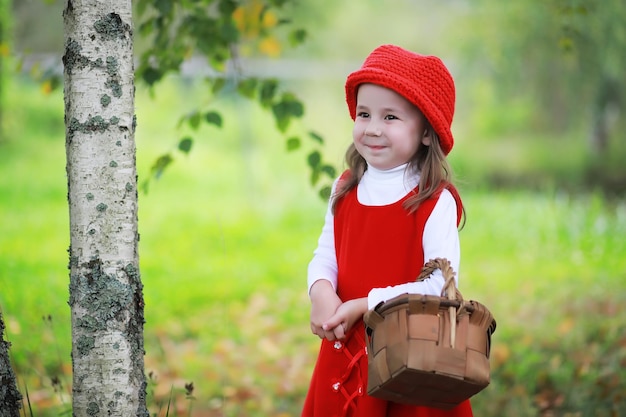 Une petite fille avec un chapeau rouge et des robes marche dans le parc. Cosplay pour le héros de conte de fées "Le petit chaperon rouge"