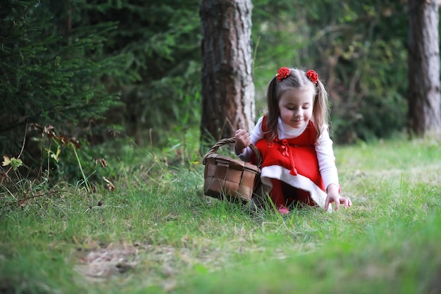Photo une petite fille avec un chapeau rouge et des robes marche dans le parc. cosplay pour le héros de conte de fées 