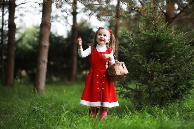 Une petite fille avec un chapeau rouge et des robes se promène dans le parc. Cosplay pour le héros de conte de fées "Le petit chaperon rouge"